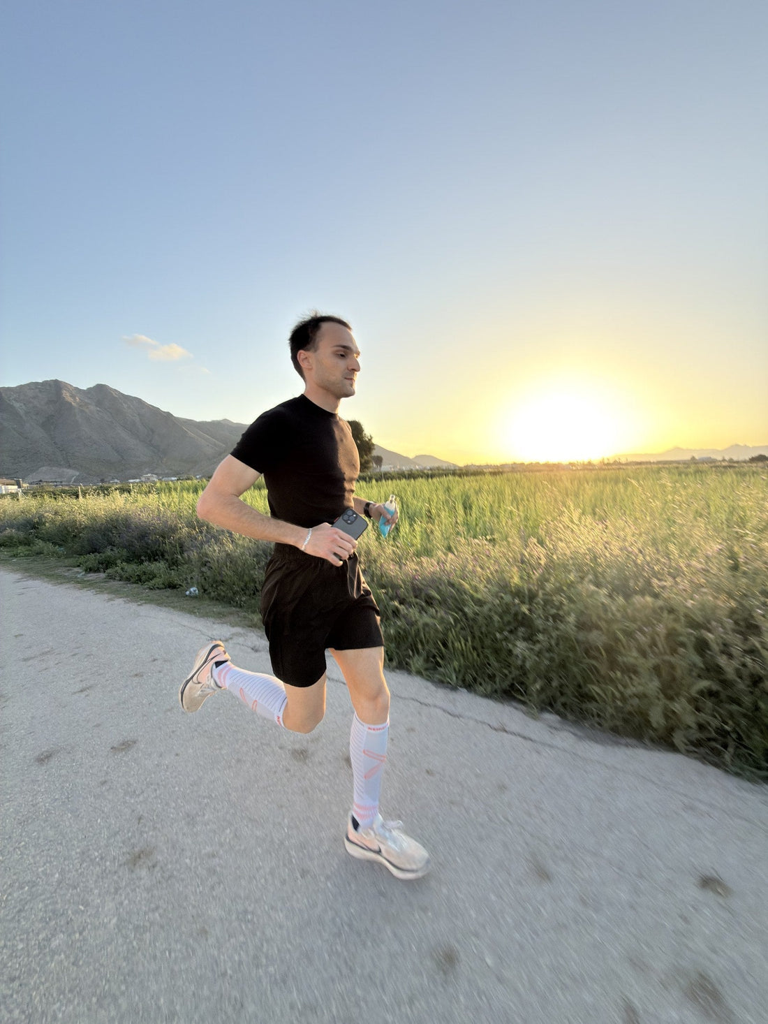 Runner corriendo por un camino de tierra al atardecer con calcetines de compresión Kompresion